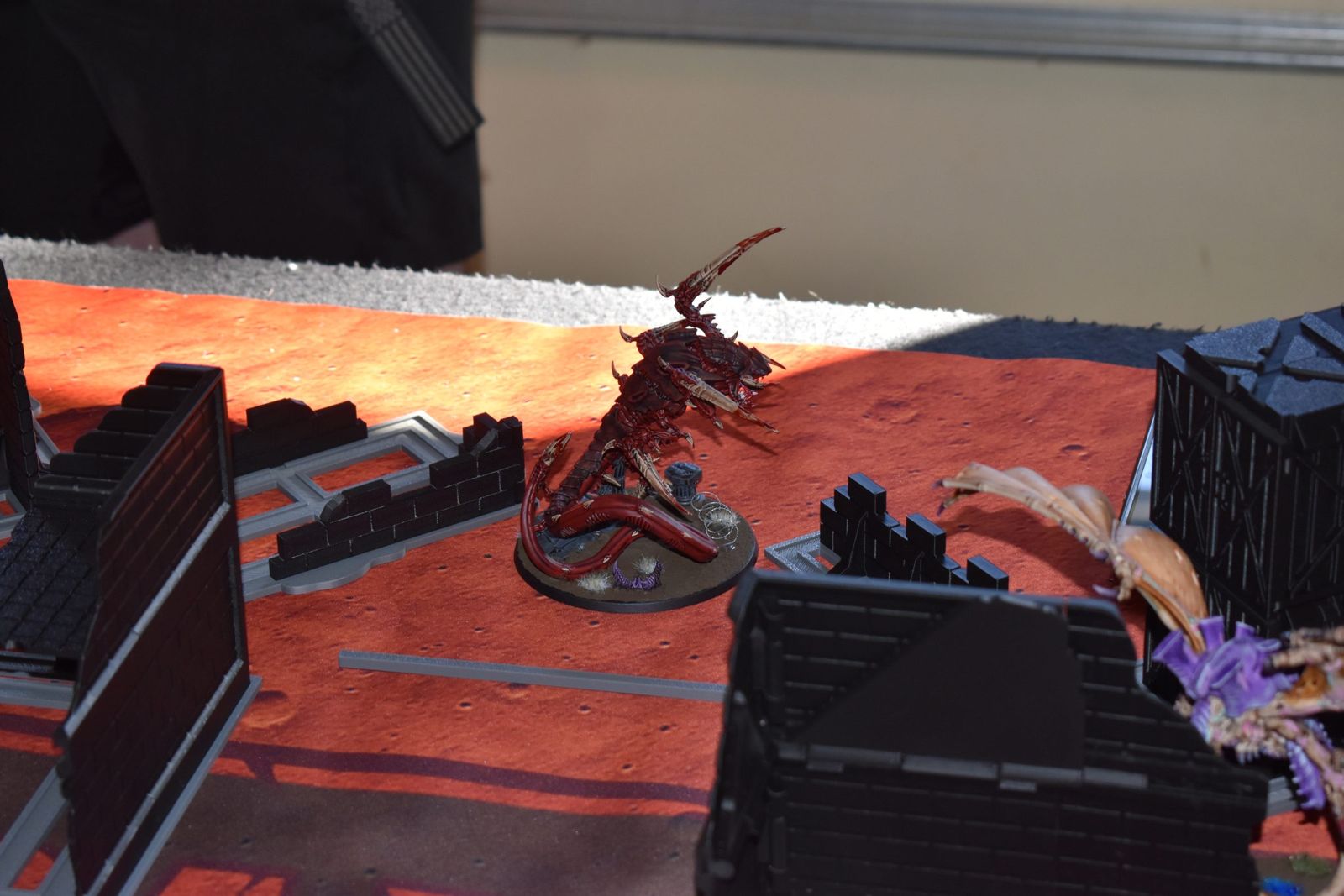 Painted models moving between 3D-printed ruins on a red battlefield mat